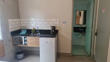 Une cuisine compacte équipée d’un four à micro-ondes, d’un évier et d’une machine à café. Une petite poubelle se trouve sous le plan de travail.