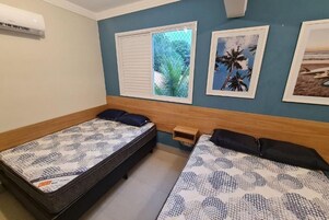 Quarto com duas camas, janela com vista para o verde e ar condicionado fixado na parede.