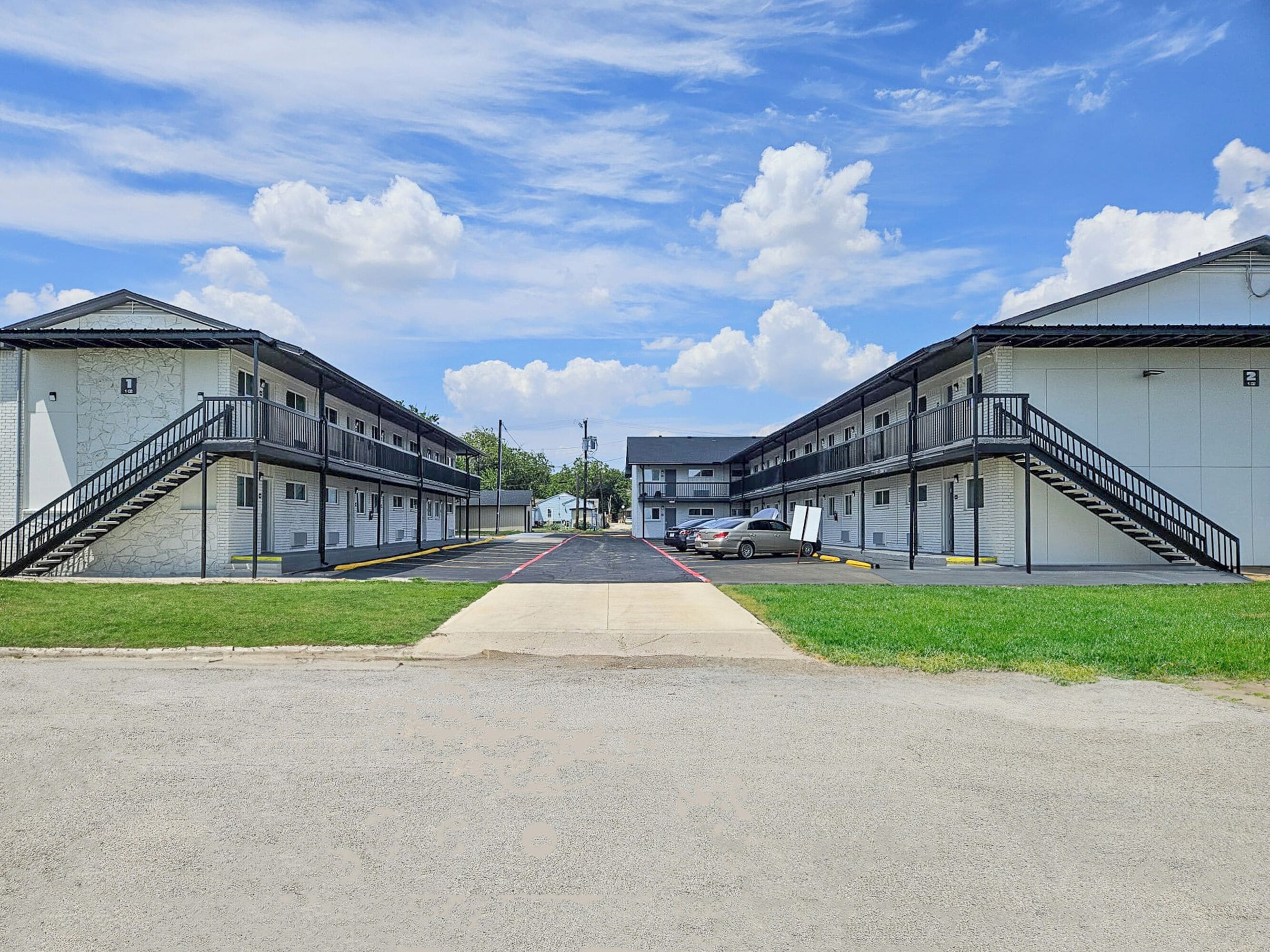 A motel with two-story buildings, a central walkway, and a parking area with cars.
