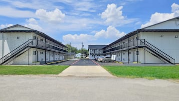 A motel with two-story buildings, a central walkway, and a parking area with cars.