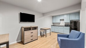 Een moderne woonkamer met een flatscreen televisie, een houten kast, een klein tafeltje en een blauwe bank.
