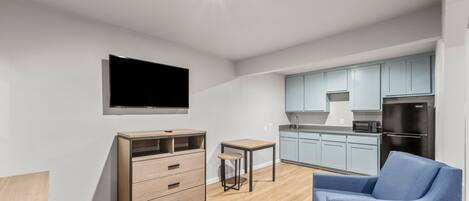 A modern living room with a flat-screen TV, a wooden cabinet, a small table, and a blue sofa.