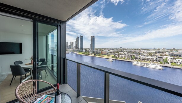 A modern balcony with a city view, a dining area with chairs, and a table with a bottle and magazine. - Melbourne Corporate Stays – Docklands Waterfront (Docklands)