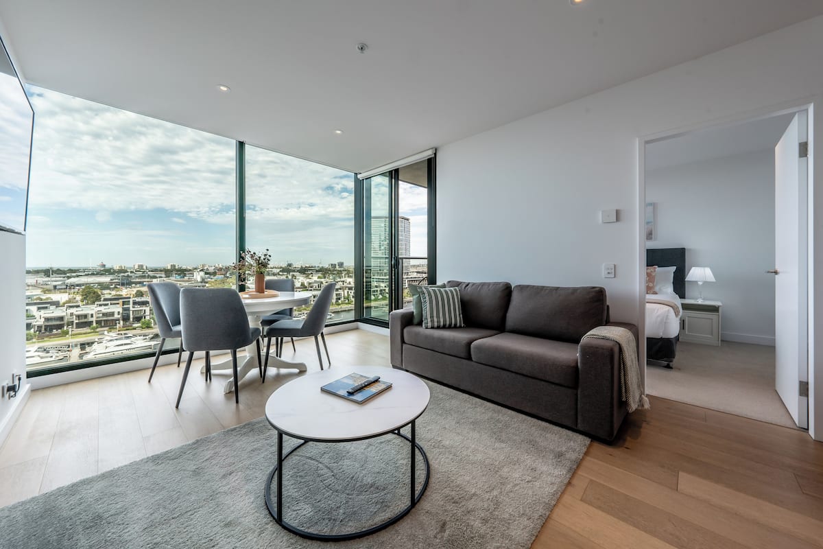 Een moderne woonkamer met een groot raam, een bank, een salontafel en een eethoek.
