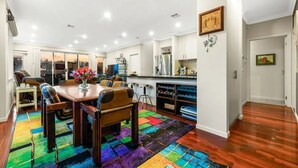 A spacious dining area with a wooden table and chairs, a colorful rug, and a kitchen area with modern appliances. - StayAU Pakenham Townhouse with Lakeview (Pakenham)