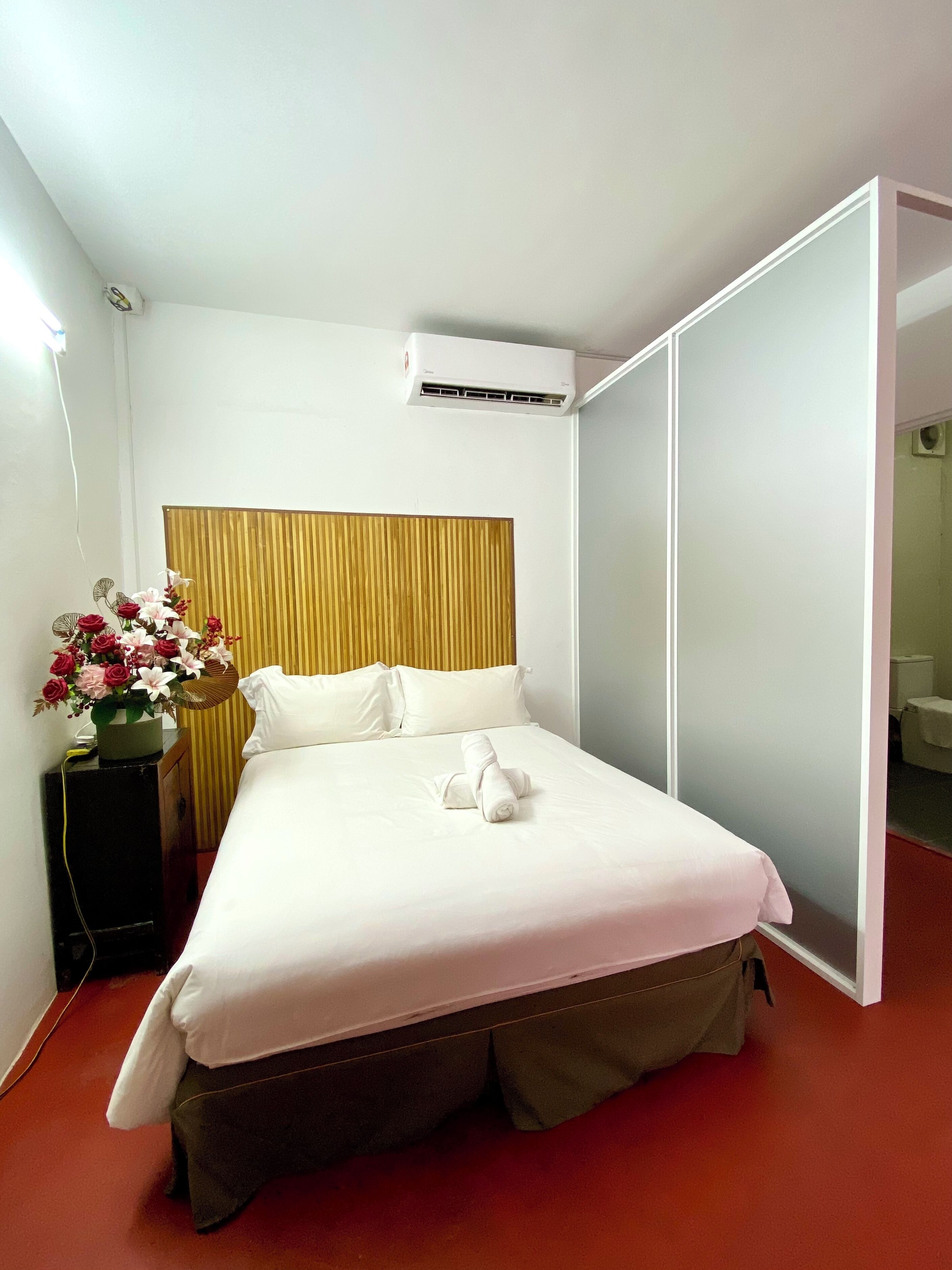 A hotel room with a bed, a wooden headboard, a bedside table with a vase of flowers, and a sliding door closet.