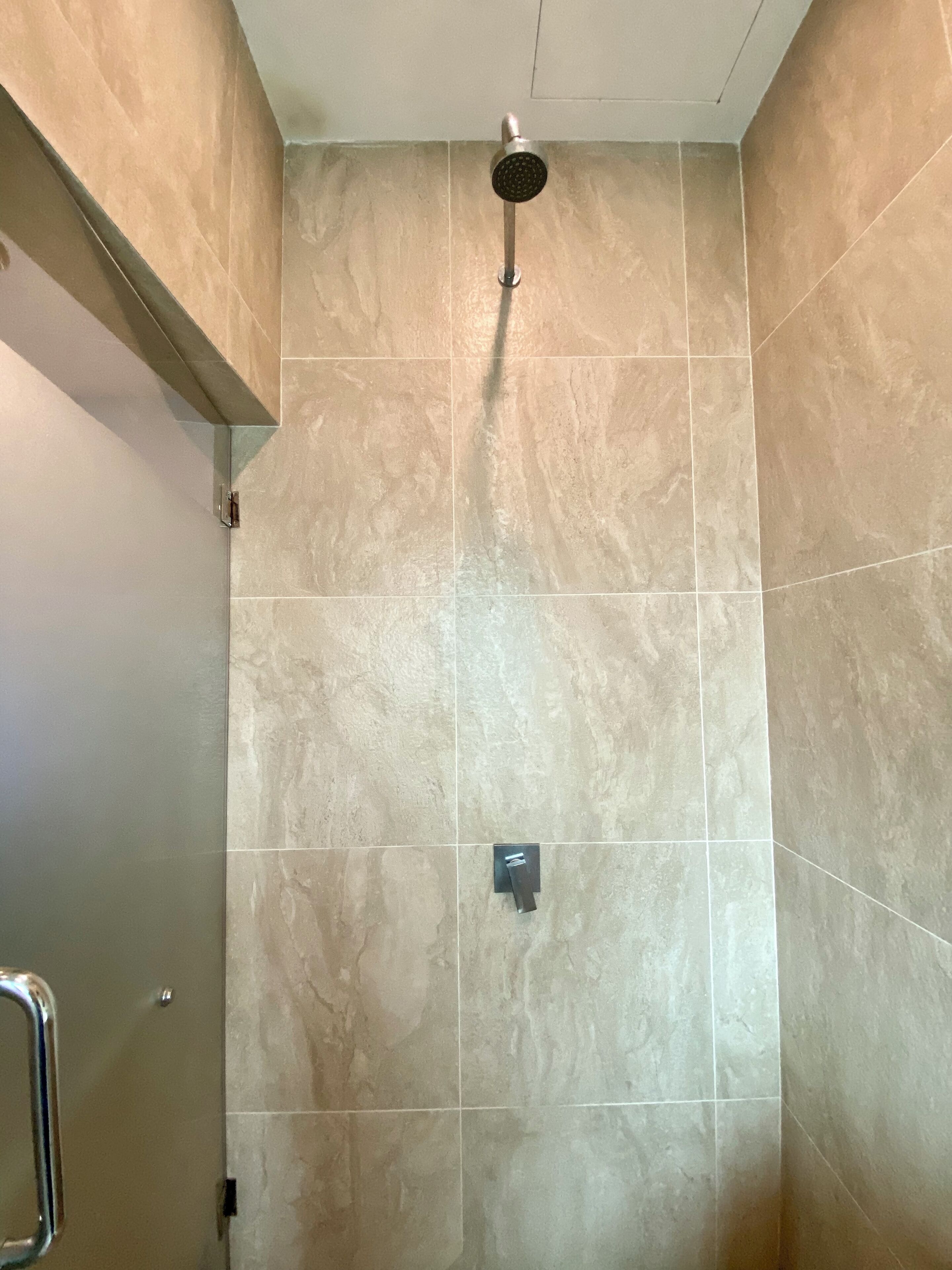 Um chuveiro com um chuveiro manual, um painel de controle e uma parede revestida de azulejos.