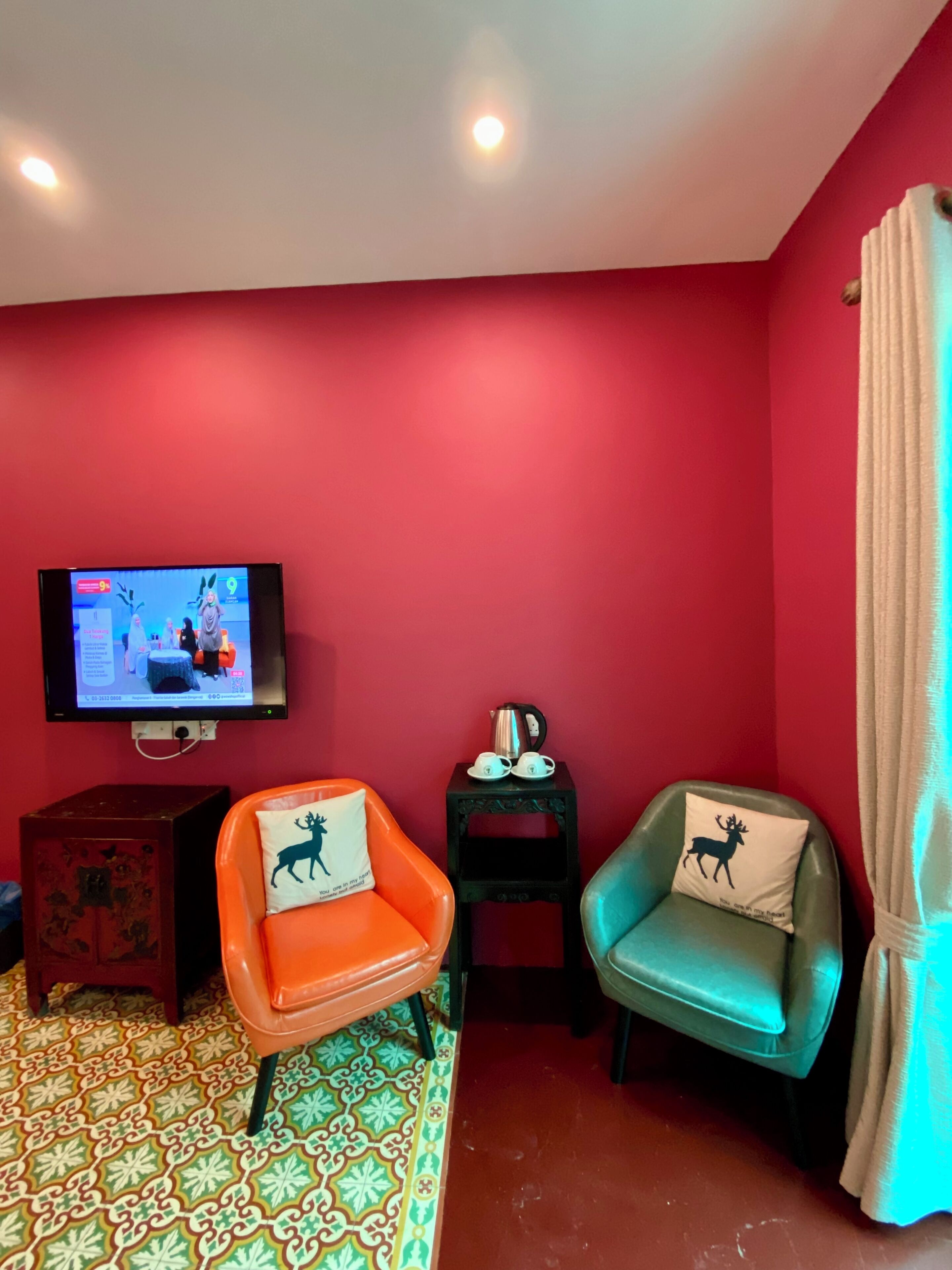 Habitación con paredes rojas, dos sillones con cojines de temática animal, una mesita con una tetera y un televisor mostrando un juego.