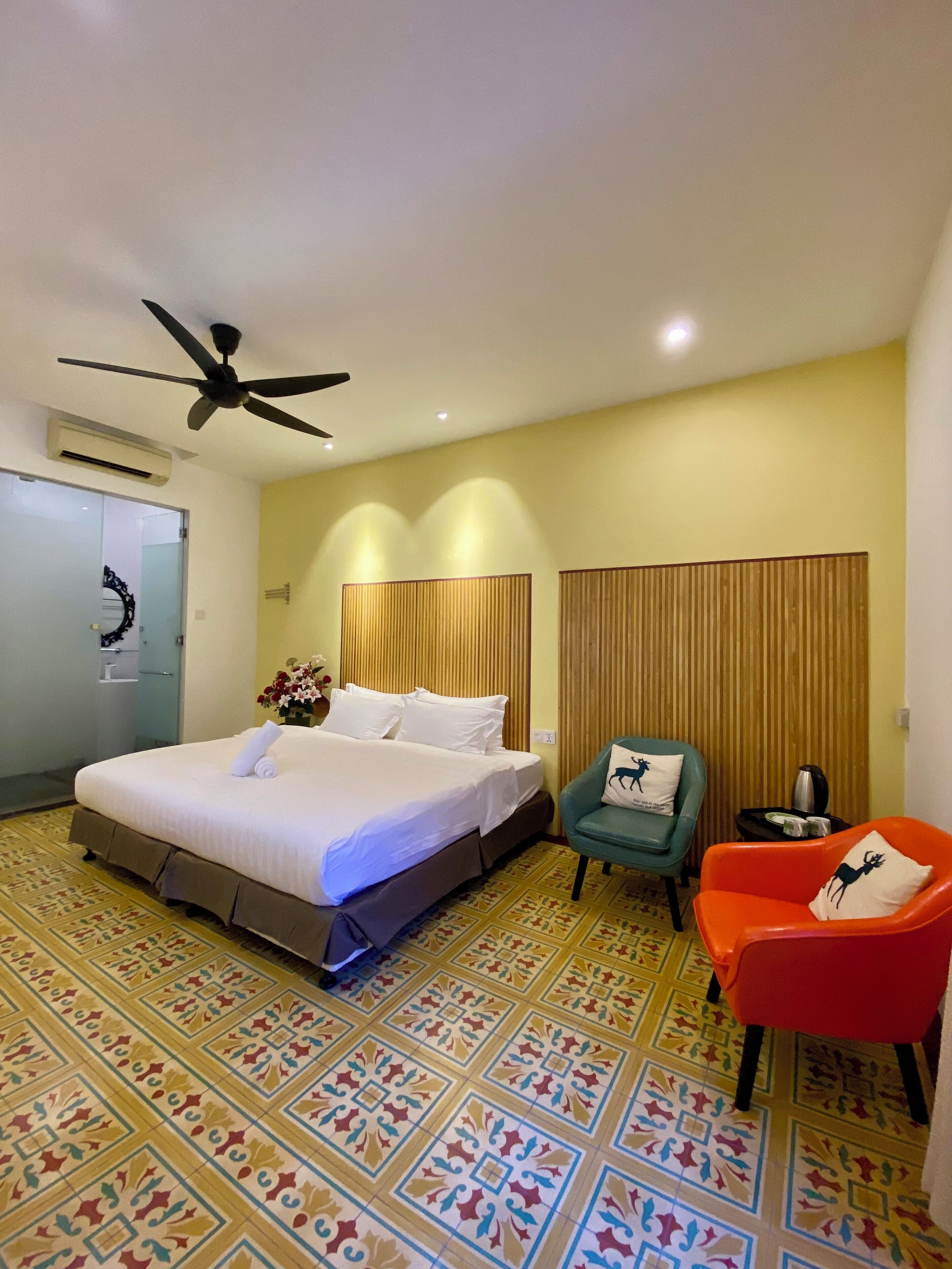 Une chambre d’hôtel avec un lit, un ventilateur de plafond, une chaise, une petite table et un sol à motifs.