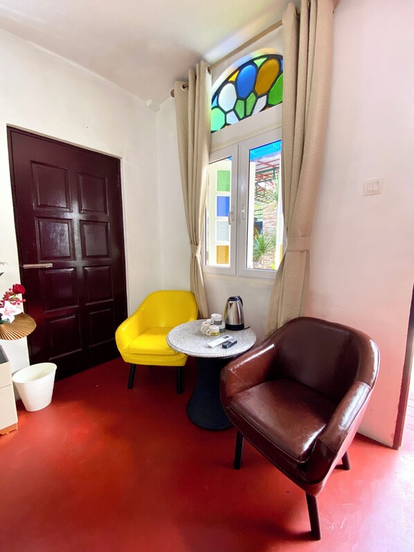 A room with a dark wooden door, a yellow chair, a brown leather chair, a small round table with a kettle, cups, and a remote control. - Bayu Bayu Hotel by Soft Loft (George Town)