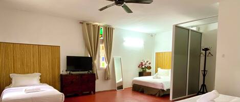 Quarto de hotel com duas camas, ventilador de teto, televisão, espelho, cabideiro e uma mesa pequena.