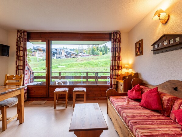 A cozy room with a wooden bed, a wooden table, two chairs, and a view of a green landscape through a large window.