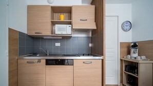 Cocina compacta con armarios de madera, microondas, máquina de café y un reloj en la pared.