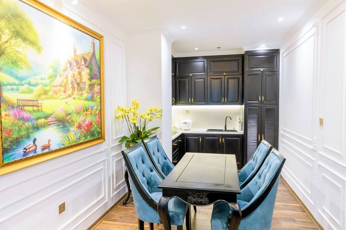 Un coin repas avec une table et des chaises, un tableau accroché au mur et une cuisine en arrière-plan.