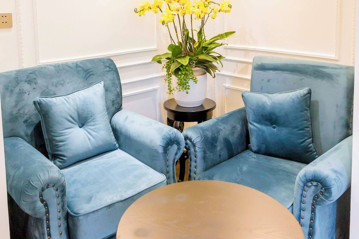 Une pièce avec deux fauteuils bleus, une table ronde en bois et une plante en pot ornée de fleurs jaunes.