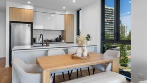Une cuisine moderne avec des meubles blancs, un plan de travail en bois et un coin repas comprenant une table en bois et des chaises blanches.