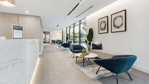 Un espace d’accueil moderne avec un comptoir en marbre, des chaises bleues et des œuvres d’art accrochées aux murs.