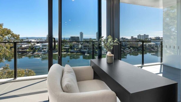 Une chambre moderne dotée d’une grande fenêtre donnant sur un port de plaisance et sur le paysage urbain.