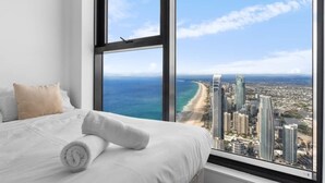 A hotel room with a large window offering a view of a beach and city skyline.