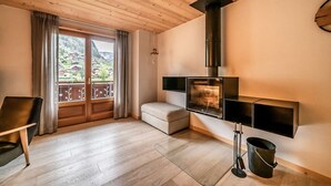 Un salon moderne avec un plafond en bois, une cheminée, un canapé et une vue sur un paysage montagneux grâce à de grandes fenêtres.