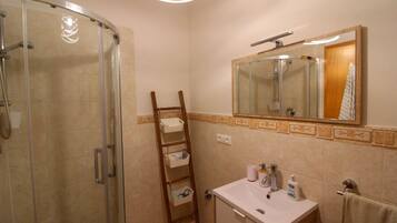 A bathroom with a glass shower enclosure, a wooden ladder, a sink with toiletries, and a mirror above the sink.