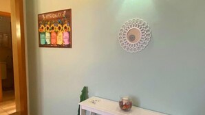 En hall med en ljusblå vägg, en dekorativ väggdekoration, en inramad skylt med solrosor och ett vitt konsolbord med hyllor.
