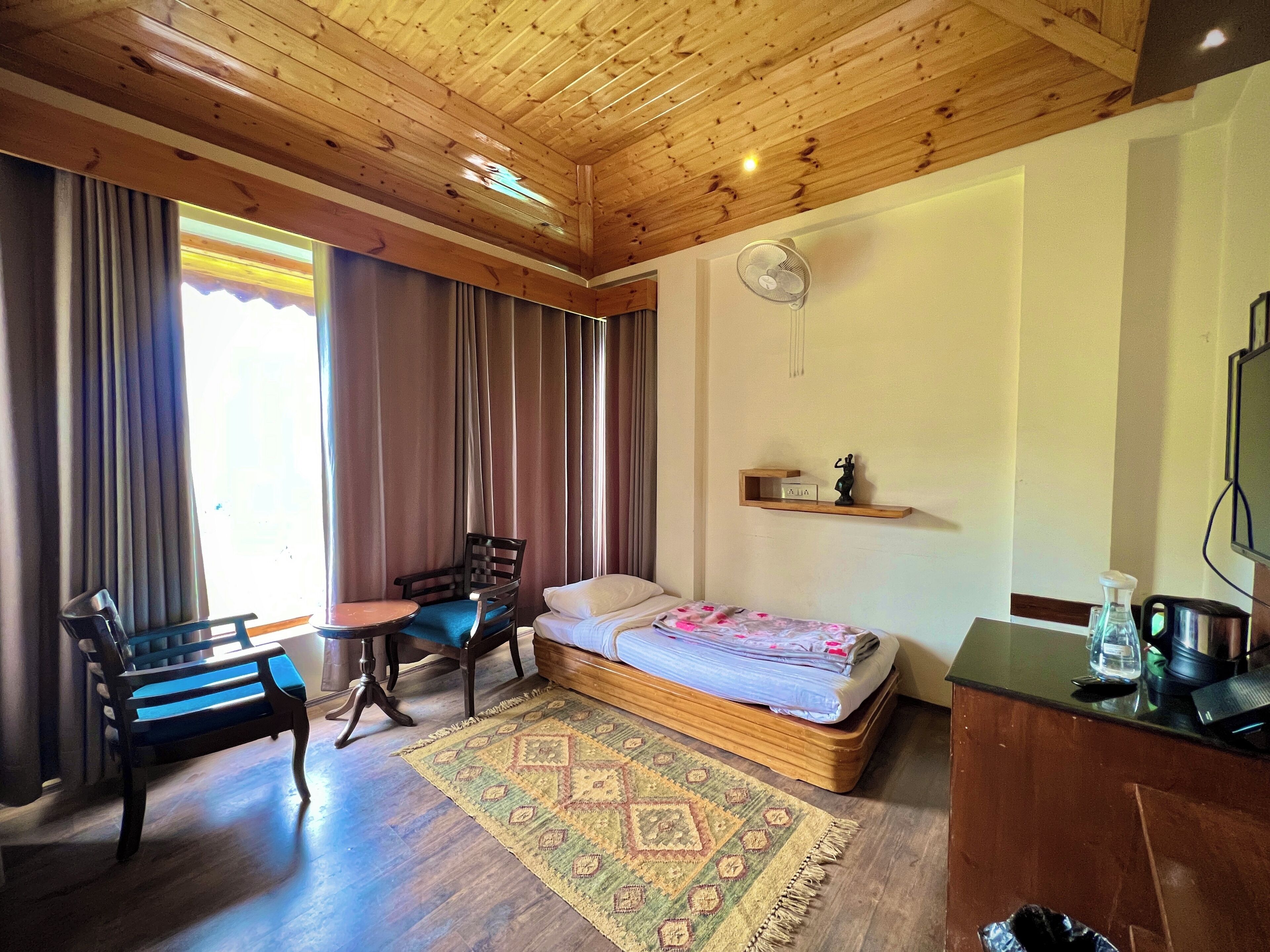 Una stanza con rivestimento in legno, un letto, una sedia, un tavolino e una ventola.