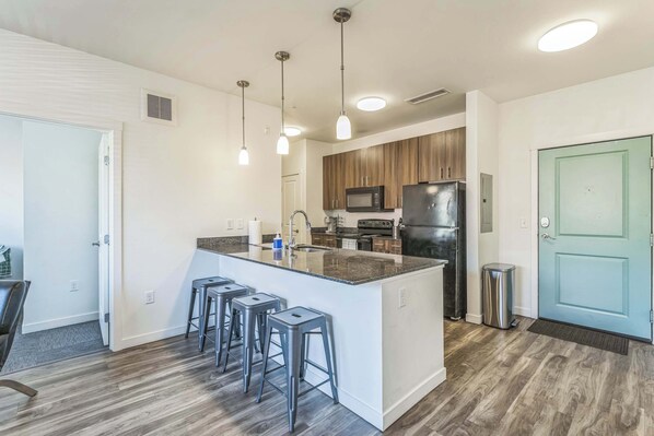 Una cocina moderna con una isla central, taburetes de bar, microondas, refrigerador y armarios de madera.