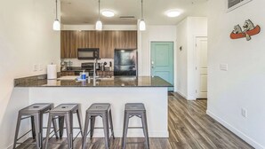 A modern kitchen with a central island, bar stools, wooden cabinets, stainless steel appliances, and pendant lighting. - Big Flat + 2 min to UM + 95 Walkscore (Missoula)