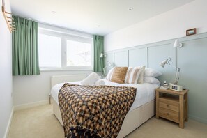 A bedroom with a bed, bedside table, lamp, and a window with curtains.