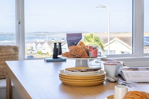 A breakfast setup with croissants, a coffee machine, and a view of the beach through a window.