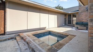 A swimming pool with stone steps, a covered patio, and a brick wall.