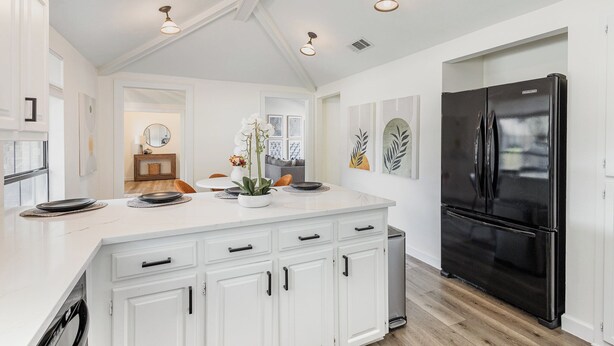 A modern kitchen with white cabinetry, a black refrigerator, and pendant lighting.