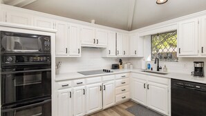 A modern kitchen with white cabinetry, a built-in microwave, oven, and dishwasher, a window with a view, and a gray rug on the floor.