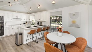 A modern kitchen with white cabinets, a central island, and orange chairs around a white table.