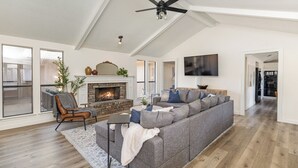 A spacious living room with a large gray sectional sofa, a fireplace, and a ceiling fan.