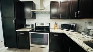 Una cocina compacta con armarios oscuros, un horno de acero inoxidable, un microondas y un tostador.