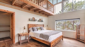 Un dormitorio con cama de madera, una mesita de noche, una ventana con vistas a árboles y techo de madera.
