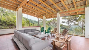 Un espacio al aire libre cubierto con sofá, sillas y una mesa, con vista a un paisaje montañoso.
