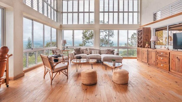 Un amplio espacio habitable con grandes ventanales, suelo de madera, un conjunto de sofás y una televisión.