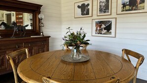 Une table de salle à manger ronde en bois, ornée d’un vase de fleurs au centre, entourée de chaises en bois.
