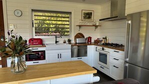 Une cuisine moderne avec des meubles blancs, des appareils en acier inoxydable, un plan de travail en bois et une fenêtre donnant sur un paysage verdoyant.