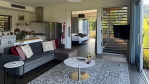 Un salon moderne avec un canapé gris, une table basse et un coin cuisine visible à travers une porte ouverte.
