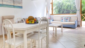 A dining area with a table set for four, a sofa with patterned cushions, and a large window with curtains. - Casa Cris - Beach House By LVH (Puerto del Carmen)