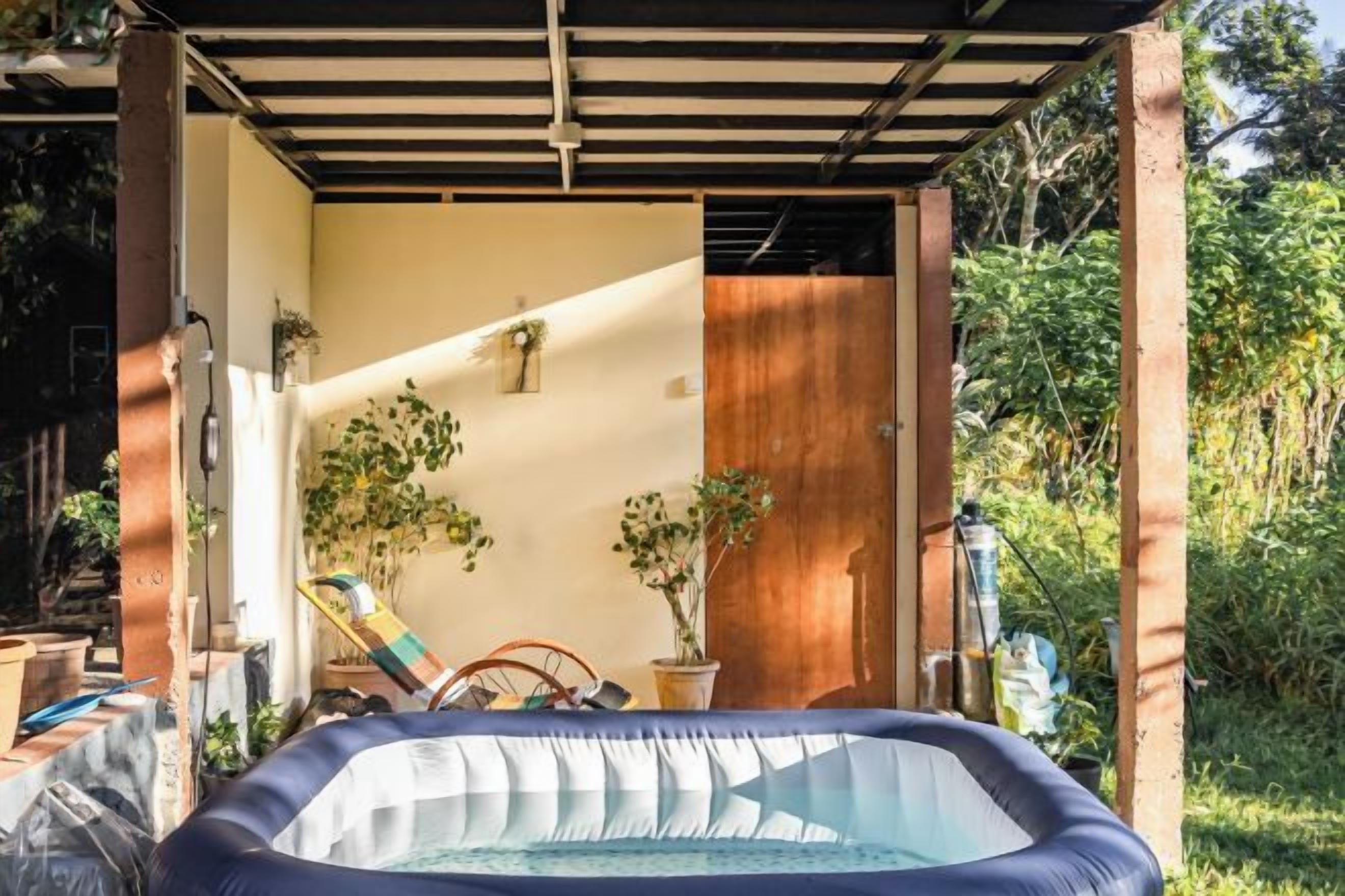 Ein Außenbereich mit Whirlpool, überdacht von einer Pergola, umgeben von Kübelpflanzen und einer Holztür.