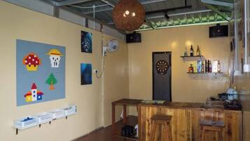 A bar area with a dartboard, shelves with bottles, and a wooden counter.