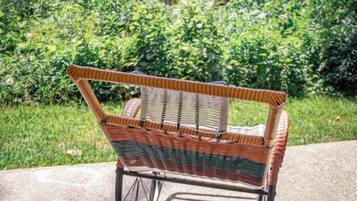 A wicker chair with a metal frame, positioned outdoors with a green hedge in the background.
