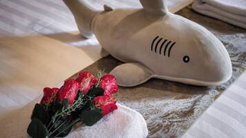 A plush shark toy on a bed with a towel and a bouquet of flowers.