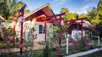 A house with a red roof and white walls, surrounded by a garden with pink flowers and a white picket fence.