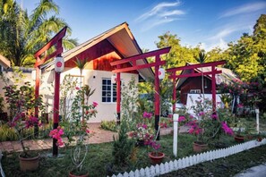 Ein Haus mit rotem Dach und weißen Wänden, umgeben von einem Garten mit rosa Blumen und einem weißen Zaun.
